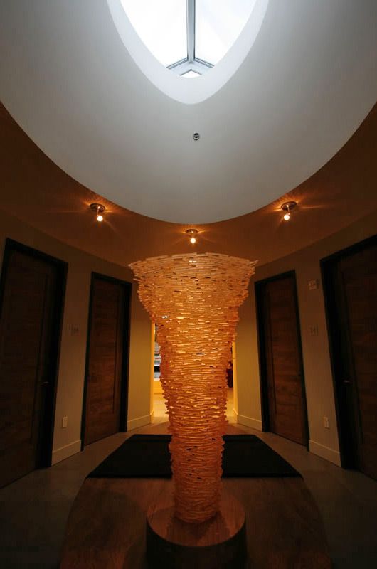 Tall stacked sculpture in a dim hallway beneath a skylight, with warm wall lights and dark doorways on both sides
