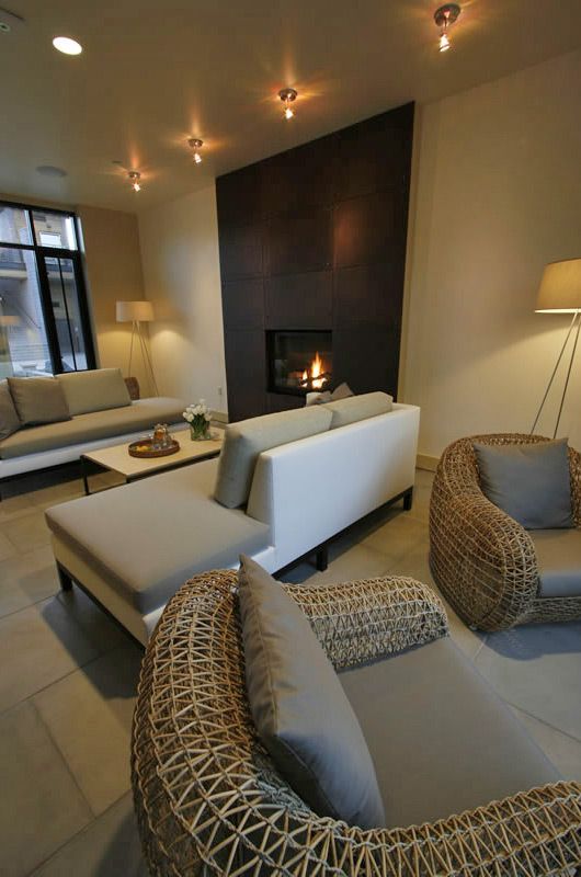 Modern living room with white sofa, wicker chairs, soft lighting, and a fireplace on a dark accent wall