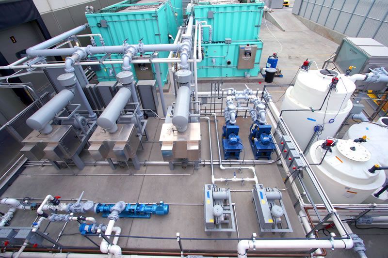 Industrial plant with teal tanks, silver piping, and blue pumps on a rooftop platform