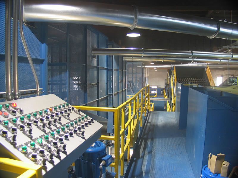 Industrial control room with blue machinery, yellow railings, and large ventilation ducts