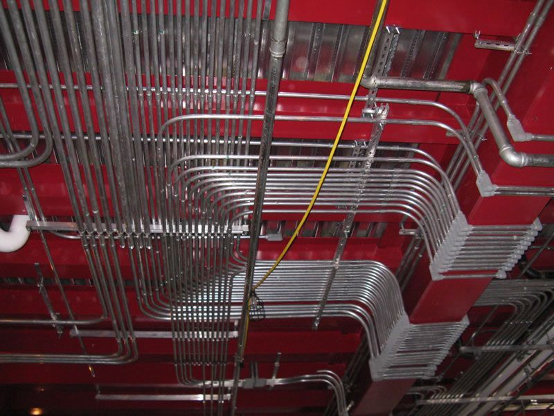 Red ceiling with rows of silver metal conduit pipes and a yellow cable running through them