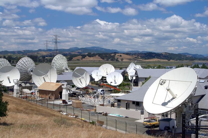 Large satellite dish array in a rural field with hills and cloudy sky