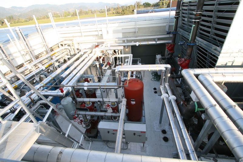 Industrial rooftop with white pipes, red equipment, and workers in a metal utility area