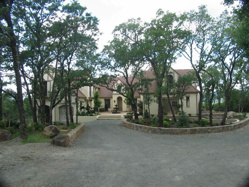 Large house with arched entrance, surrounded by trees and a gravel driveway