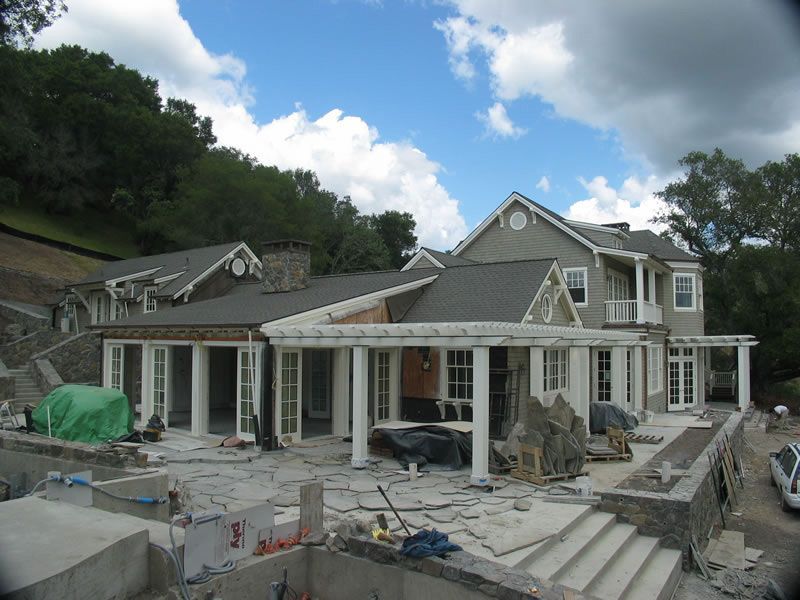 House under construction with stone facade, scaffolding, and unfinished front steps under a cloudy sky