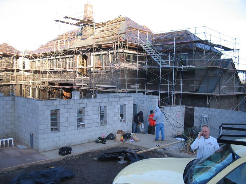 Construction site with a house under scaffolding and workers near a partially built stone wall
