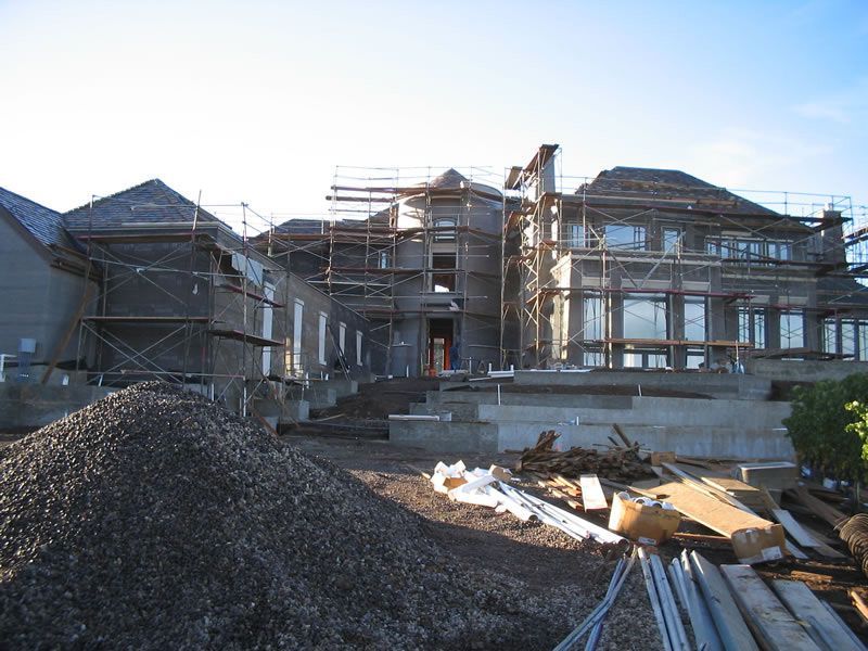 Partially constructed house with scaffolding, piles of gravel, and building materials under a clear sky