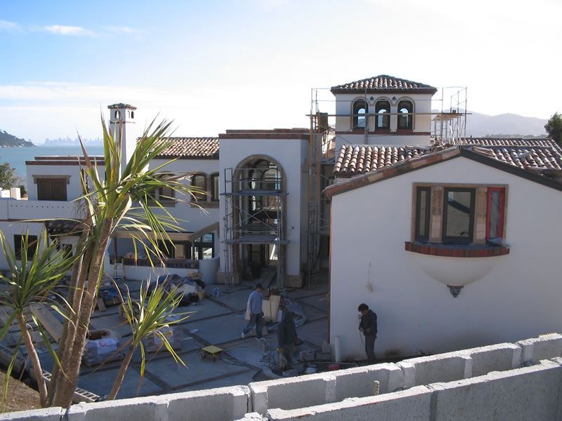Mediterranean-style building courtyard with palm trees, arched entry, tiled roofs, and a person by the wall