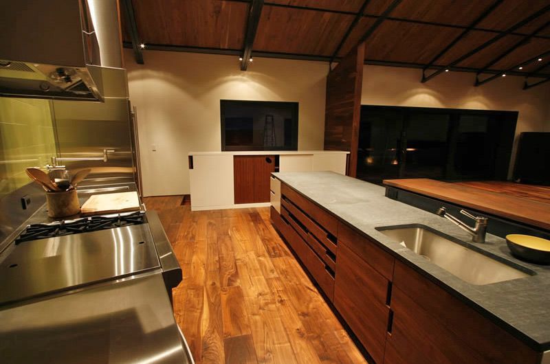 Modern commercial kitchen with stainless steel counters, wooden floors, and an island under warm lighting
