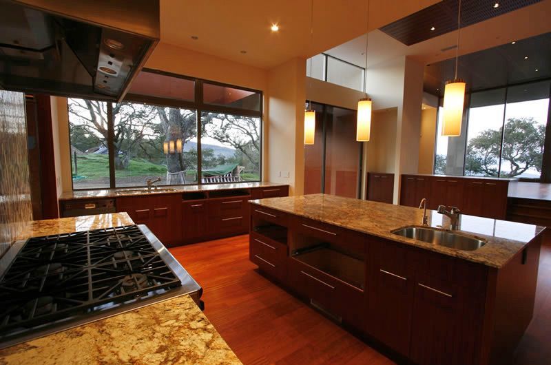 Modern kitchen with dark wood cabinets, granite island, and large windows overlooking trees and water