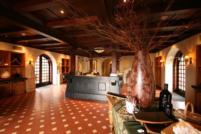 Warm restaurant interior with arched windows, red tile floor, and a central bar under tree-like decor