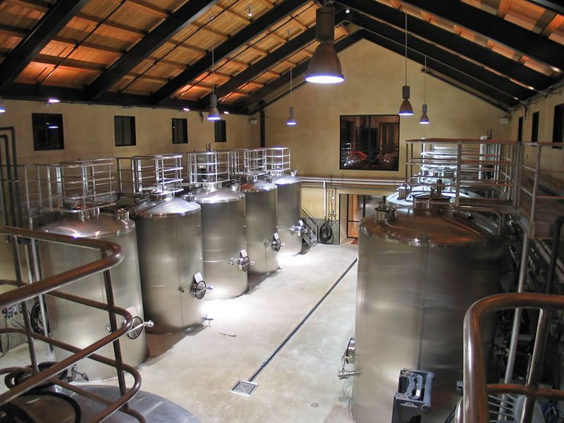 Large stainless-steel fermentation tanks in an industrial brewery with a high wooden ceiling and overhead lights