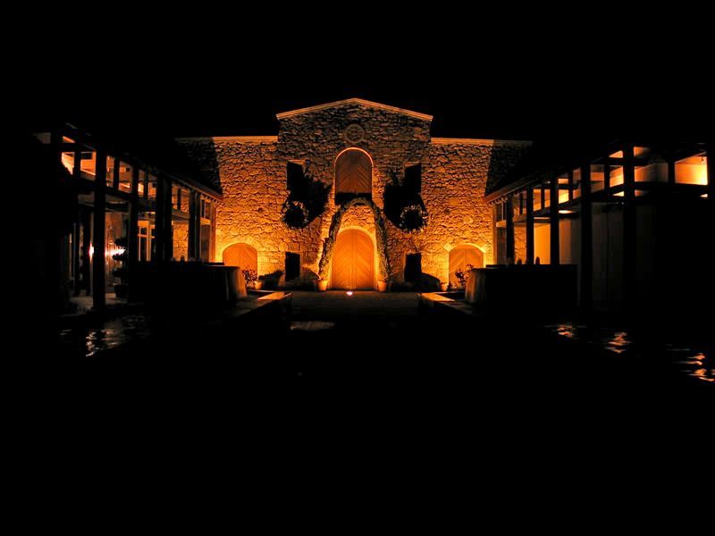 Illuminated stone building courtyard at night with warm orange lighting and dark surrounding windows