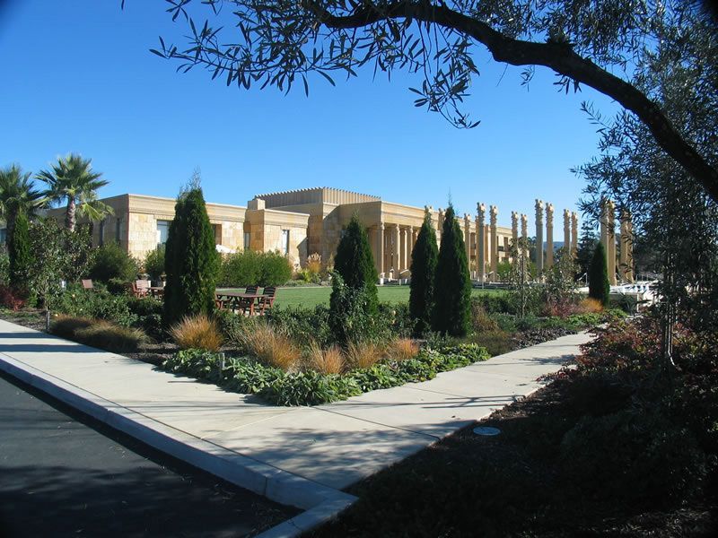 Landscaped garden with stone paths and tall cypress trees in front of a beige building under a blue sky