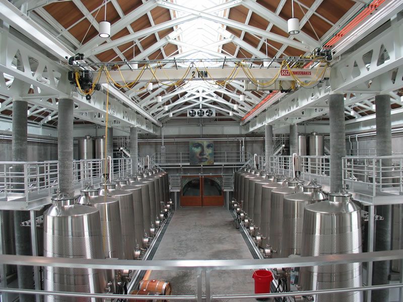 Rows of stainless steel fermentation tanks in an industrial brewery with a high white steel ceiling