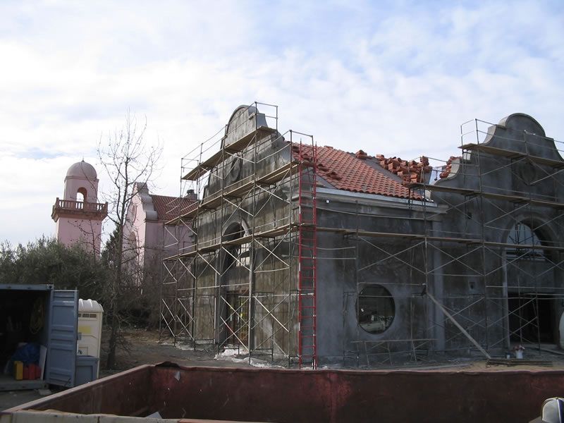 Scaffolding surrounds a stone building with a red-tiled roof under renovation.