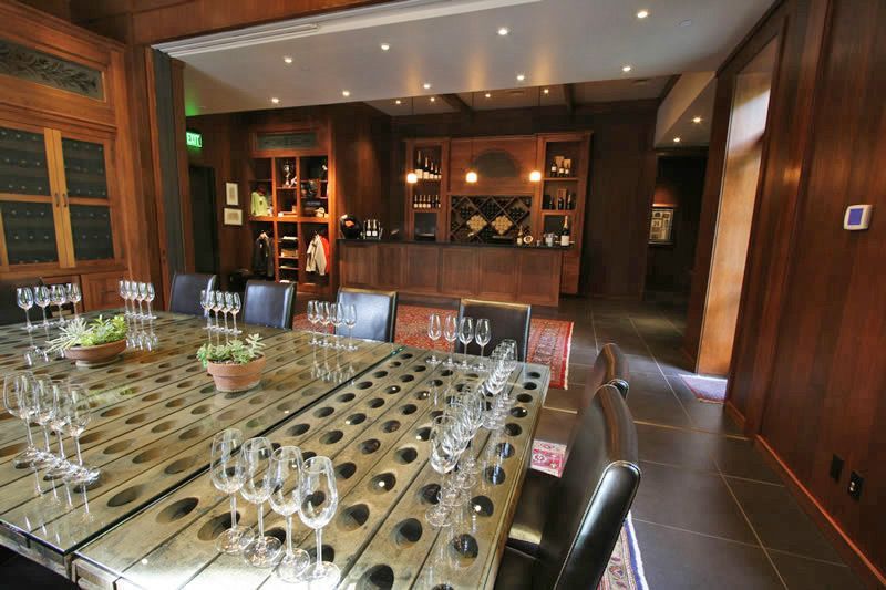 Modern dining room with a long glass table, chairs, wood-paneled walls, and recessed lighting