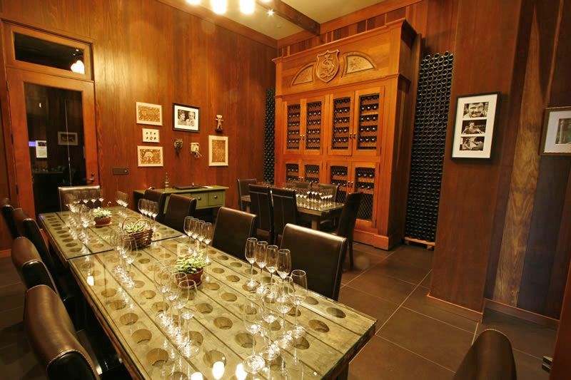 Wood-paneled wine cellar dining room with a long glass table and upholstered chairs