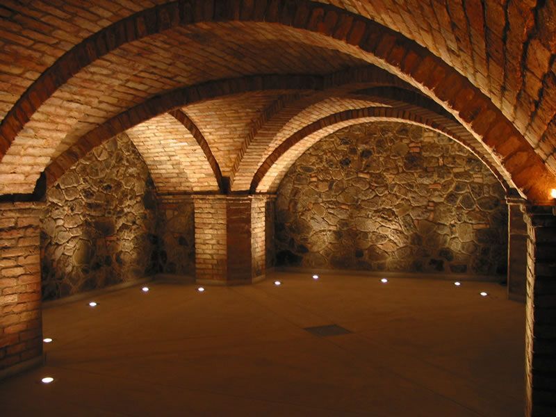 Stone vaulted room with arched brick ceiling, rough walls, and small floor lights.