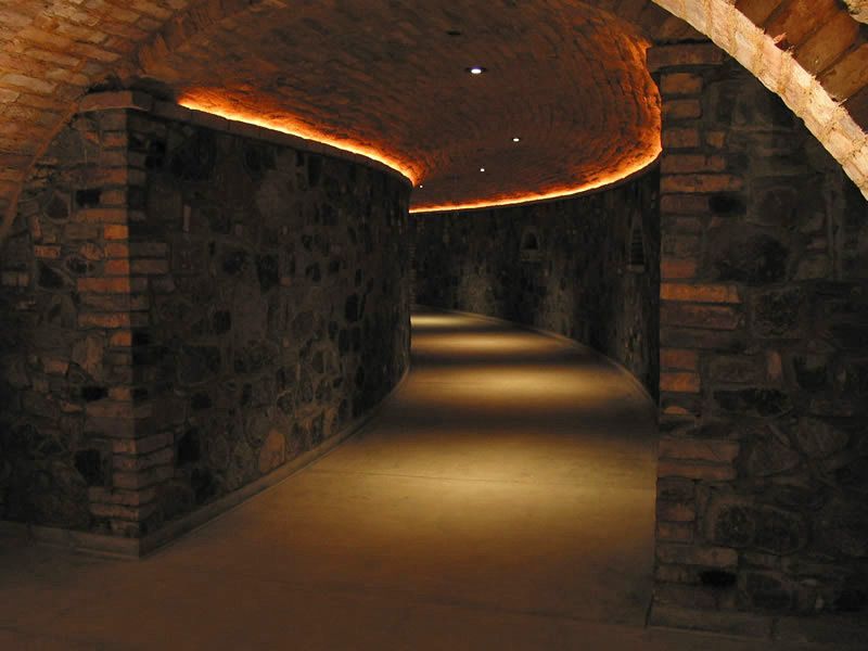Dim stone corridor with warm orange ceiling lights and a winding path