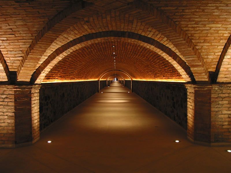 Long brick-arched underground tunnel with warm lights and a vanishing point in the distance