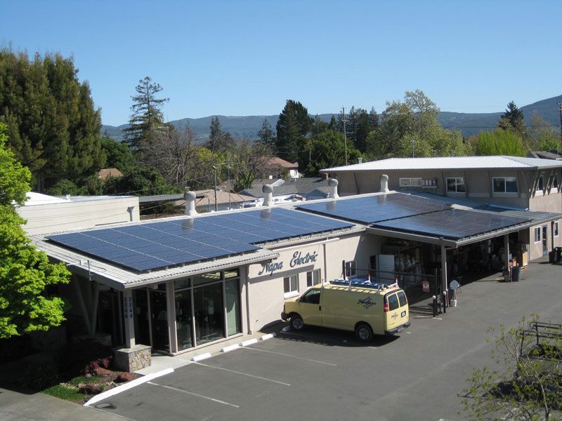 Small roadside building with solar panels, parked van, and wooded hills in the background