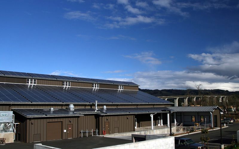 Solar panels on a low building under a blue sky with clouds.