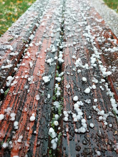 Snow and ice pellets scattered over a weathered red wooden deck surface