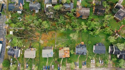 Aerial view of suburban homes with green yards and a line of parked cars along a street
