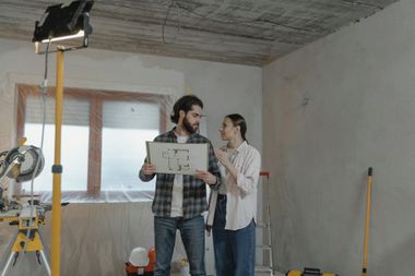 Two people reviewing plans in a partially renovated room with construction tools and a work light.