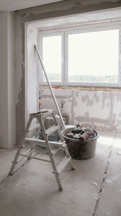Renovation room with ladder, bucket, and a large window with stripped walls.