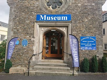 Stone museum entrance with blue signs and flags on either side of the doorway
