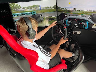 Person driving a racing simulator with a steering wheel and pedals, wearing headphones and seated in a red chair.