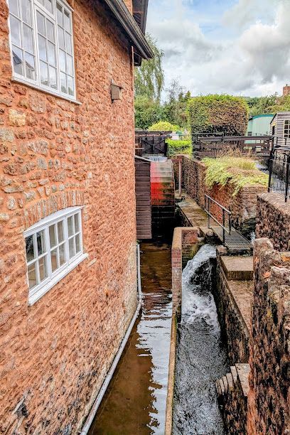 Narrow water channel beside a red brick building and stone wall, with steps and greenery ahead
