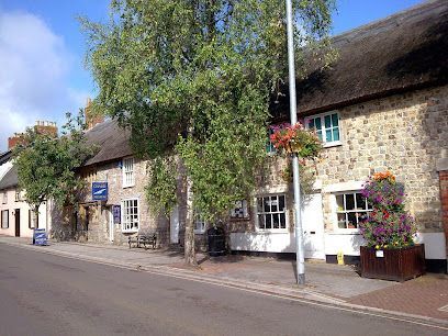 Stone cottages with thatched roofs, flower baskets, and a quiet village street under a blue sky