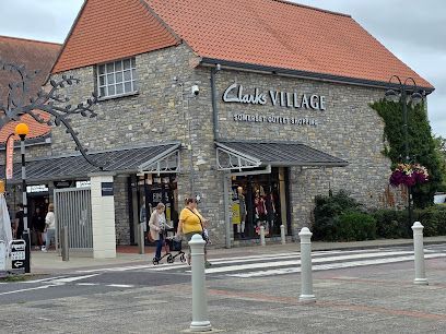 Exterior of Clark’s Village shopping center with stone walls, red roof, and people near the entrance