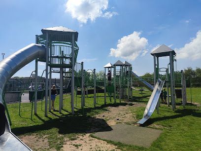 Outdoor playground with metal climbing towers, slides, and green grass under a blue sky
