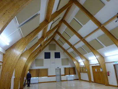 Empty hall with curved wooden beams and white walls; one person stands near the left side.