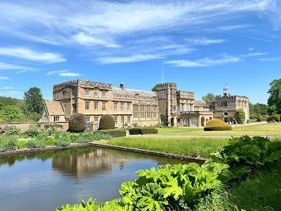 Historic stone manor beside a pond, with green lawn and bright blue sky.