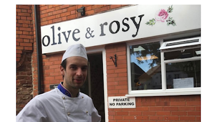 Chef standing outside Olive & Rosy restaurant sign on a brick building