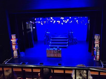 Blue-lit theater stage with steps, props, and columns, viewed from the audience.