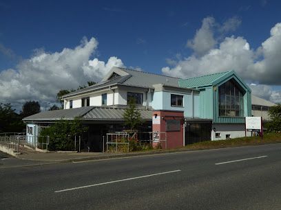 Roadside two-story building with teal roof and red entrance under a cloudy blue sky