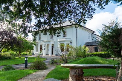 White two-story house with large windows, framed by green lawn and trees in a sunny garden
