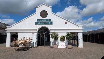 White market building with a turquoise sign, potted plants, and outdoor seating under a cloudy sky