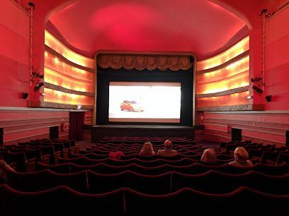 A dimly lit movie theater with red seats and a bright screen at the front