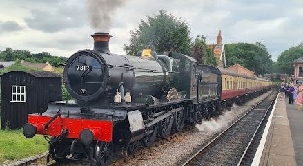 Black steam locomotive pulling passenger cars at a rural train station platform