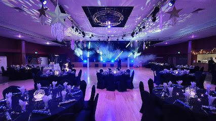 Elegant banquet hall with round tables and purple stage lighting, set up for an event.