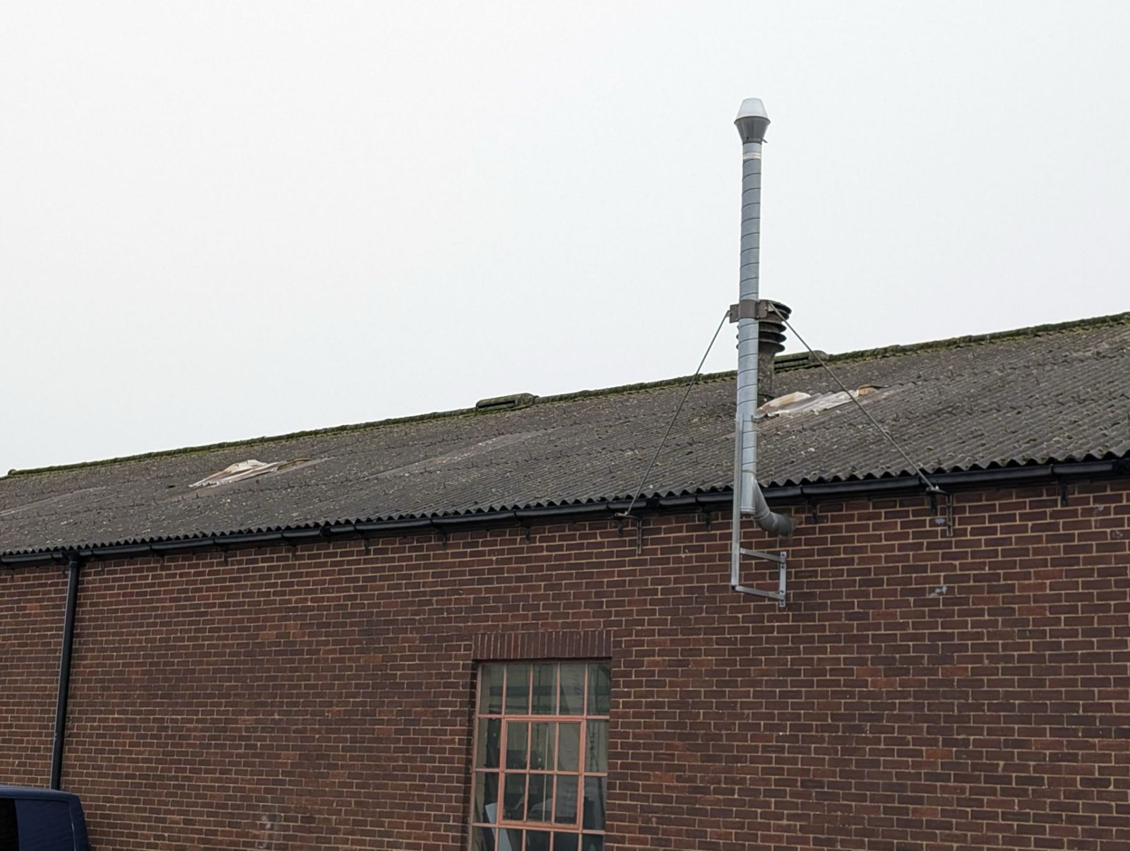 Brick building roof with a vertical metal chimney stack against a pale sky