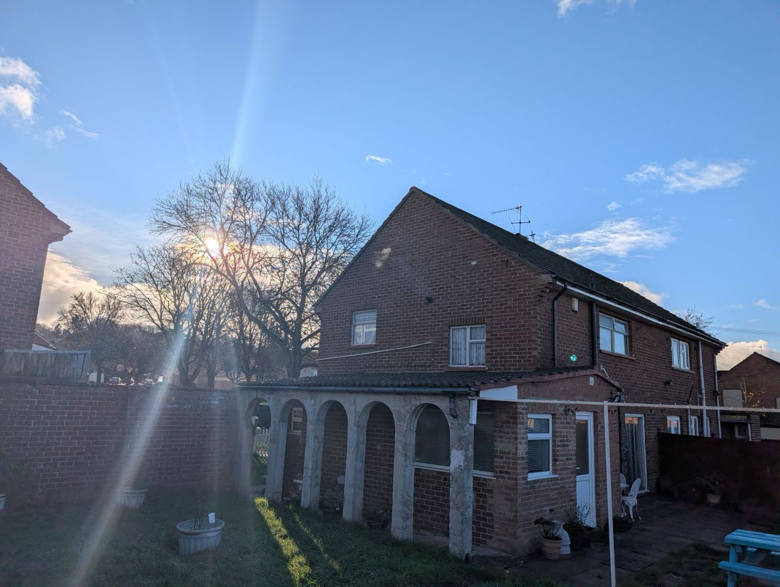 Brick house with white arched porch in a sunny backyard under a blue sky