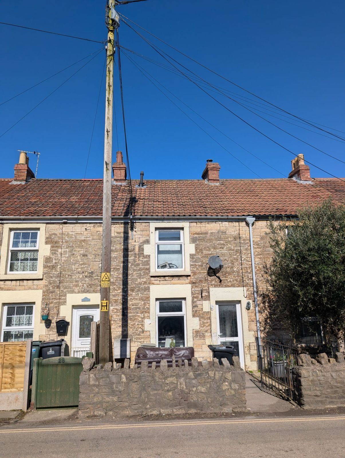 Row of stone terraced cottages with red roofs under a clear blue sky, with a utility pole in front.